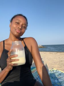 Cierra holding a mason jar of raw milk while enjoying the beach. She looks peaceful. She discovered raw milk while on the carnivore diet. 